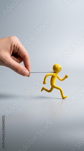 Hand pulling running yellow clay figure on gray background, career motivation, career advancement, business success, promotion, reaching goals, business development