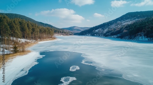 Aerial View of a Partially Frozen Lake Surrounded by Snowy Pine Forest in Winter