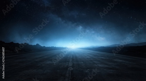 Empty asphalt road stretching into a starry night sky with distant horizon glow