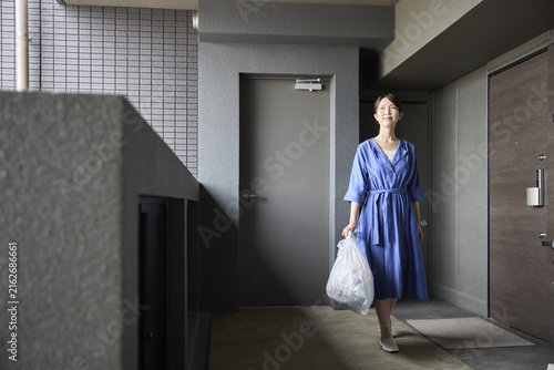 マンションの廊下でゴミを運ぶ女性