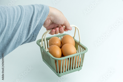 Hand holding small green plastic basket filled with brown chicken eggs isolated on white