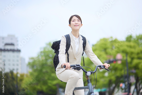 広い道路を自転車で走る会社員女性