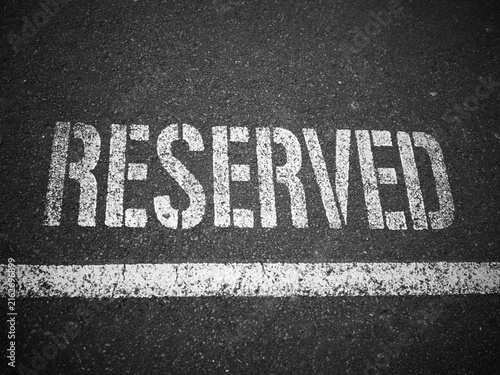 Fotografie White stencilled RESERVED marking on dark asphalt with painted line, black and w