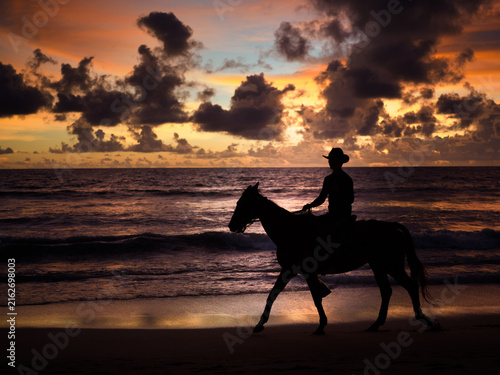 Horse and rider silhouette against vivid red and orange sunset sky, tropical beach, Thailand