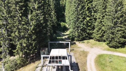 Aerial view of an abandoned chairlift station and clearcut line through dense pine forest in the mountains
