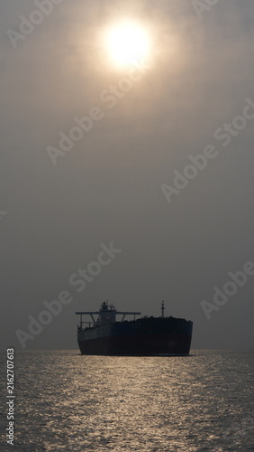 Cargo Ship at Sea with Sun Reflection and Hazy Sky