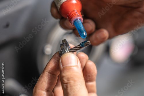 Mechanic applying blue threadlocker fluid to bolt thread before motorcycle engine assembly
