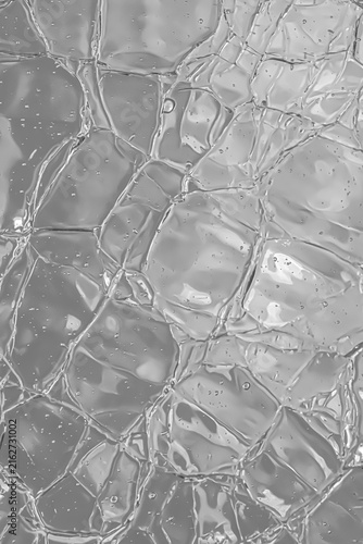 Close-up of transparent textured glass, gray monochrome surface with irregular reflections and abstract pattern