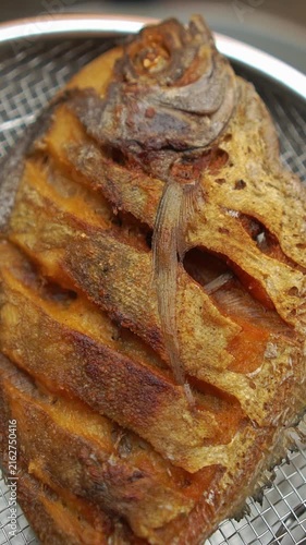 Cooking Thai fried black pomfret (Pla Jalamed Dam Thod Nam Pla). Deep-frying whole fish until crispy, simmering palm sugar with fish sauce, and drizzling over top.