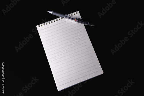 Blank lined spiral notepad and pen placed on a black background