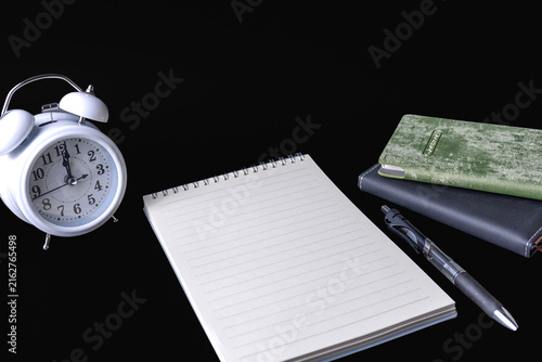 Office desk setup with blank lined notepad alarm clock and pen on black background