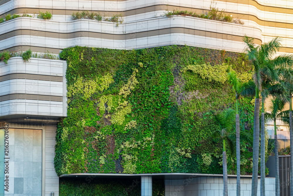 Naklejka premium Modern building facade with green living wall and integrated landscaping in Hong Kong city. Sustainable architecture, climate-conscious development, urban greening, biophilic design
