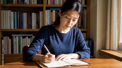 Naklejka 手帳に書き込む女性 本棚のある部屋と窓の光 予定を立てる時間