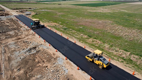 Aerial view of heavy machinery paving a new asphalt road at a construction site.