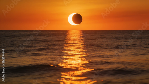 High-resolution professional stock photo of partial solar eclipse at sunset over open ocean with powerful golden reflection on water.