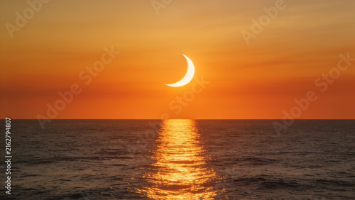 High-resolution professional stock photo of partial solar eclipse at sunset over open ocean with powerful golden reflection on water.