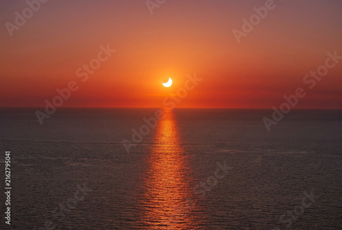 High-resolution professional stock photo of partial solar eclipse at sunset over open ocean with powerful golden reflection on water.