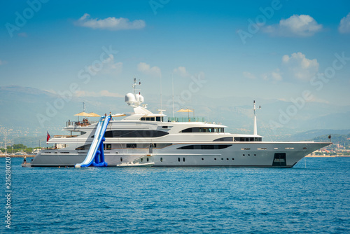 Big white superyacht anchored in the bay of Cannes, south of France during summertime with an inflatable water slide for entertainment of charter guests 