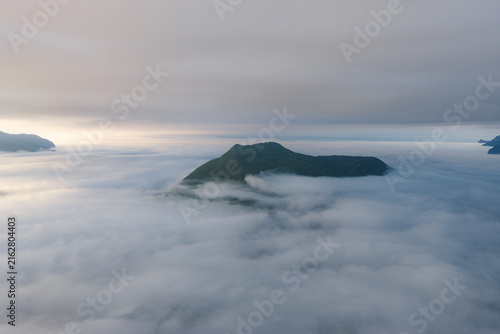 Aerial view of a mountain peak rising above a thick layer of clouds in Unalaska, Alaska, United States.