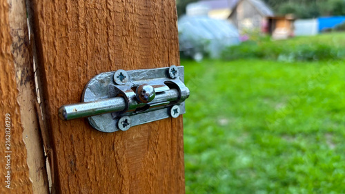 Obraz na plátne Close-up of metal barrel bolt latch installed on wooden door with green garden b