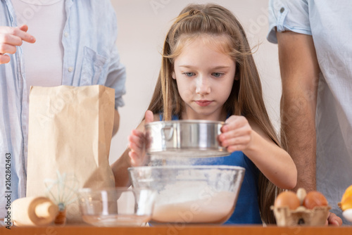 Canvas Print Young focused girl child baking in kitchen with family sifting white flour throu
