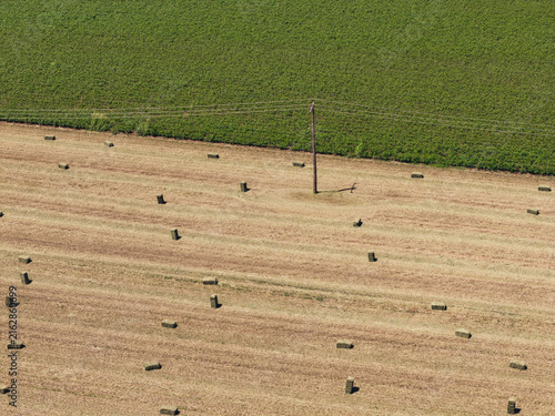 Aerial view of a harvested field scattered with hay bales and a single utility pole, adjacent to a lush green field in Greece.