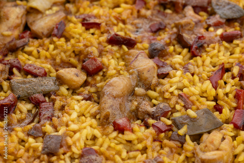 Close-up of traditional paella cooking, showing yellow rice, chicken pieces, and vegetables