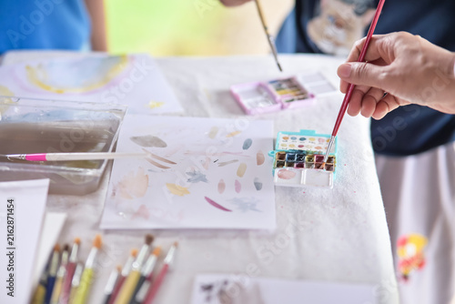 Children and teacher painting with watercolors, paintbrushes, and palette set on paper. Art education, creativity, and leisure activity concept.