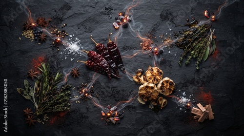 Aromatic culinary herbs and spices with smoke on black slate surface