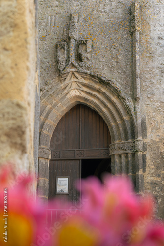 Фотография Portail gothique en pierre de l'église de Bazens avec fleurs au premier plan