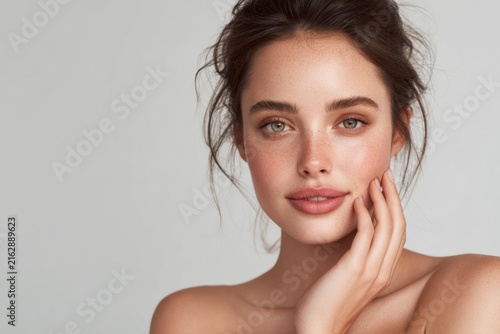 Beautiful woman with radiant skin gently touching her face in a minimalist studio setting showcasing natural beauty and elegance
