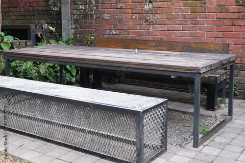 Konstfotografi Empty industrial-style outdoor table and metal bench seating positioned beside a red brick wall in a casual urban patio setting