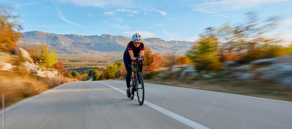 Fototapeta premium Female Cyclist Riding Road Bike on Mountain Road During Autumn Training Session