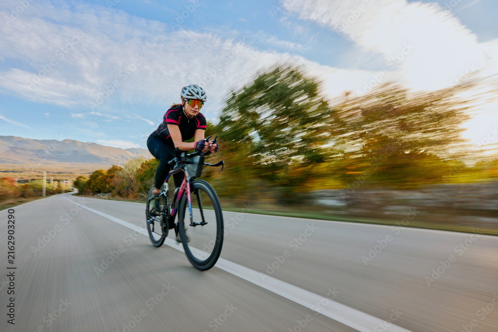 Fototapeta premium Female Cyclist Road Training At Speed Through Countryside On Racing Bike With Aerodynamic Gear