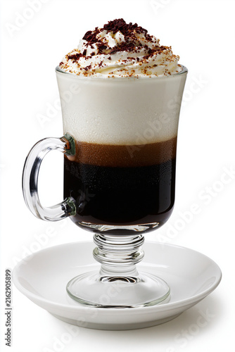 Irish Coffee sur fond blanc, servi dans un mug en verre à pied sur soucoupe blanche. Café chaud au whisky, surmonté d'une couche de crème fouettée