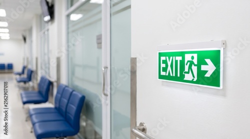Emergency Exit Sign in Corridor: A green illuminated exit sign directs people to safety in a modern, clean corridor with blue seating.