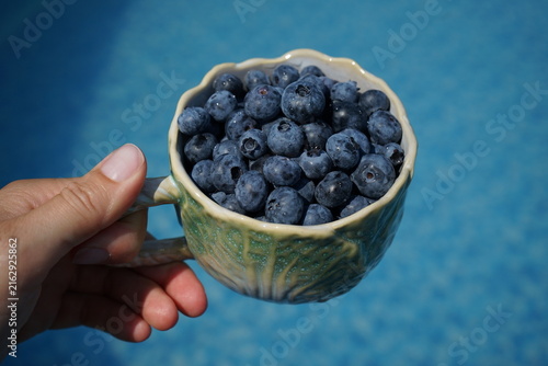 A mug filled with blueberries against the backdrop of a swimming pool.