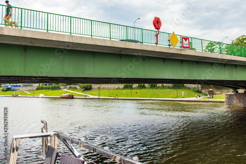 Obraz na plátne A view from a boat a side of a green metal bridge crossing over river, Green metal girder bridge spanning across the waterway