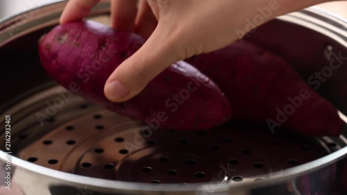 Hand putting raw purple sweet potatoes into a steamer pot to steam, Asian cooking style