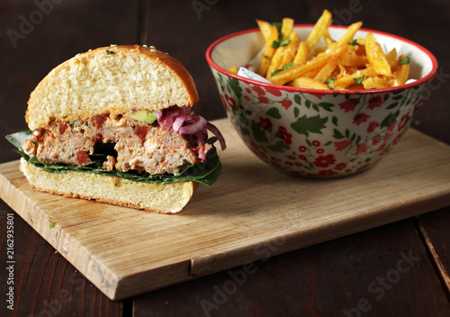 Half cut gourmet chicken burger showing juicy patty cross section with fries on the side