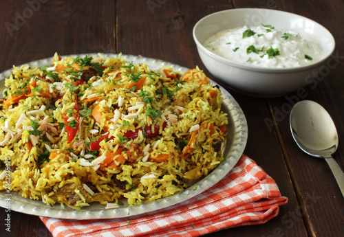 Indian chicken biryani rice garnished with flaked almonds and served with yogurt raita sauce