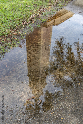 Baton Rouge, Louisiana, United States - 28 March 2023: View of the Memorial Tower at Louisiana State University reflected in a puddle on the ground with surrounding grass and pavement.