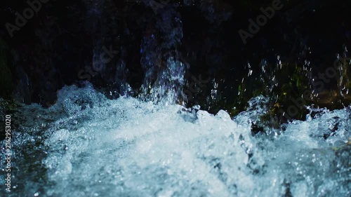 Water crashes down dark rocks. Bubbles and spray rise with force. Light glints on wet surfaces. Nature's raw energy captured in motion. Perfect for adventure or environmental themes