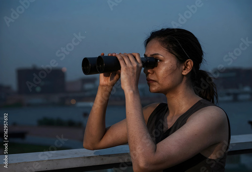 Future vision and strategic planning, woman looking through binoculars at urban landscape at dusk, business foresight and exploration