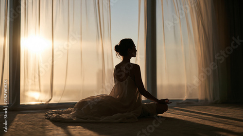 Woman Meditating in Lotus Pose by Window at Sunrise