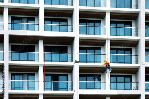 Industrial painter in safety gear working on high rise building facade. Industrial climber servicing high rise