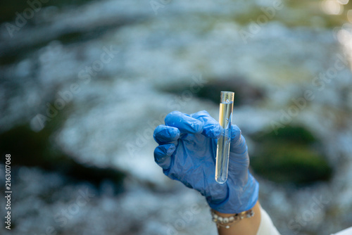 Obraz na płótnie person in blue gloves holding glass tube with water sample outdoors testing for
