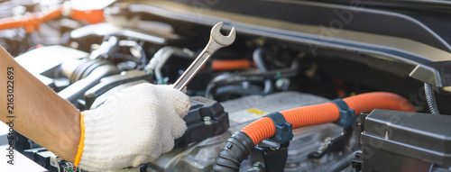 Auto mechanic hand holding a wrench during inspection and repair with electric hybrid car engine bay, professional vehicle maintenance service.