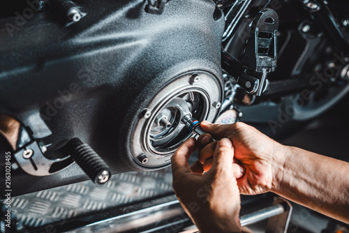 Close-up of a technician's hands using a hand ratchet tool to service and adjust motorcycle primary drive clutch assembly inside a garage workshop.
