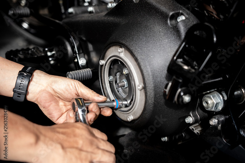 Mechanic hands using ratchet socket wrench to tighten bolts on motorcycle primary engine clutch cover